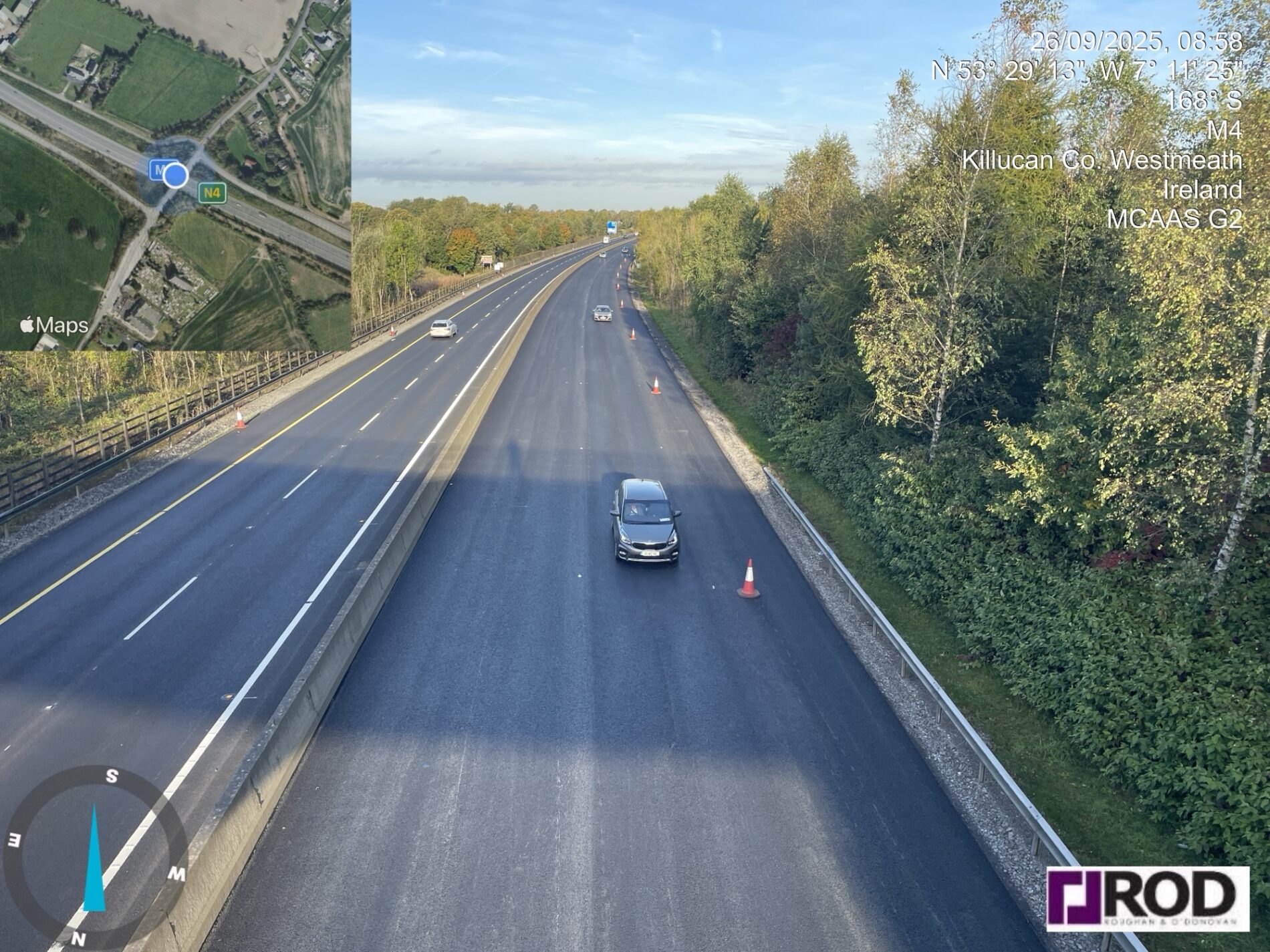 Aerial view of the M4 motorway near Killucan, Co. Westmeath, Ireland, with freshly laid asphalt and traffic cones marking a road resurfacing trial. Autumn trees line the right side of the carriageway. 